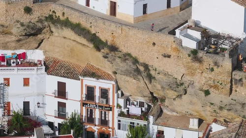 Whitewashed buildings nestle against cliffs in Setenil De Las Bodegas, Spain, featuring Bar and Cerveceria Lizon and colorful laundry on a rooftop.