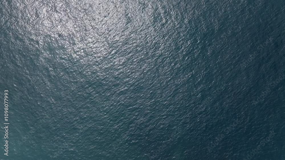 Sunlight reflects on a deep blue water surface, creating a shimmering effect with small waves dancing across the scene