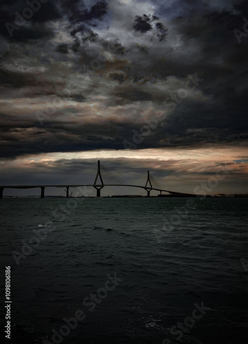 Dramatic stormy clouds over a modern cable-stayed bridge spanning across a rough sea at sunset