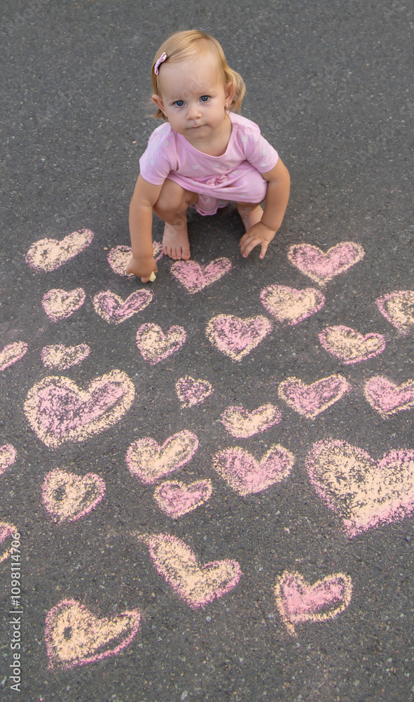 Naklejka premium child draws a heart on the asphalt with chalk. Selective focus