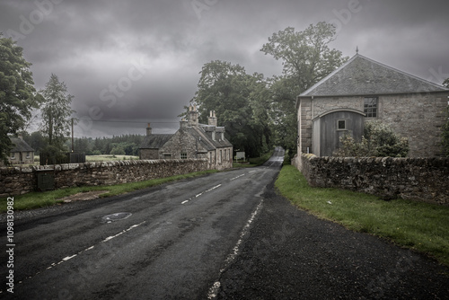 Typical old Scottish houses with walls around the property line, built with large stone blocks on a main road on a gloomy misty day in summer