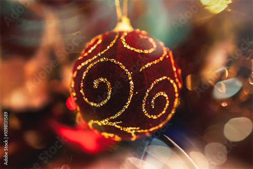 A red Christmas ornament beautifully adorned with golden swirls hangs, capturing the light in a festive displa photo