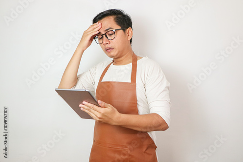 handsome barista asian man wearing brown apron and white t-shirt isolated over white background. Barista touching head suffering from headache desperate and stressed