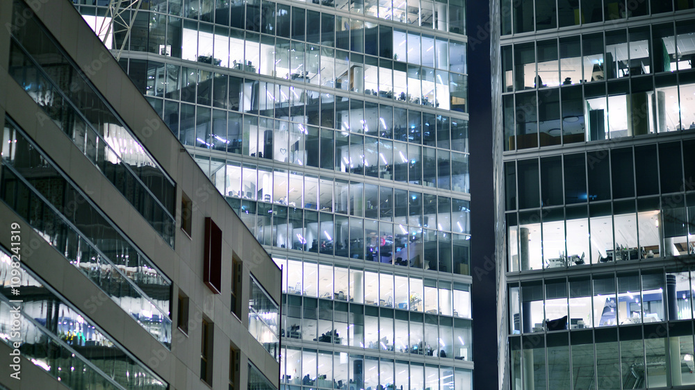 Obraz premium Office building in the evening with lightened workspaces. Modern, glazed skyscraper in financial district. Late hours in the office.