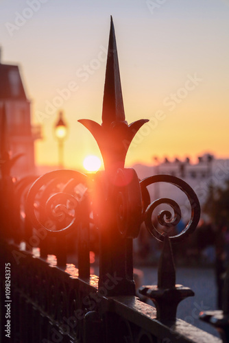 The rising sun penetrates with rays through the forged fence