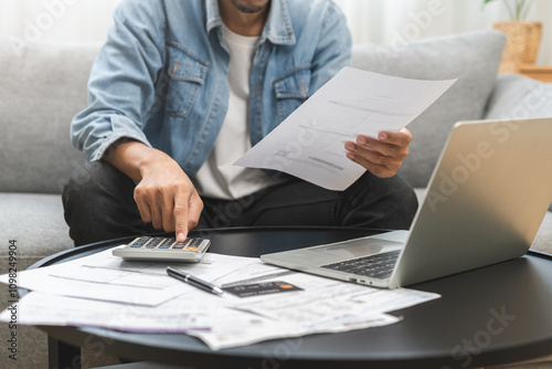 Business financial concept, owe asian young man, male sitting on couch stressed hand calculate expense on table at home from invoice or bill have no money to pay mortgage or loan, debt bankruptcy. photo