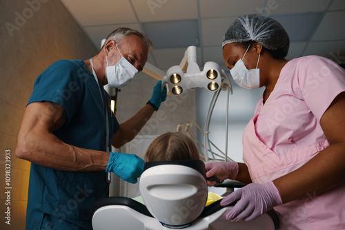 Dentist and assistant working together on dental procedure with patient at clinic. Medical professionals wearing protective masks and gloves during procedure photo