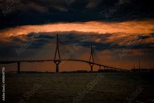 Golden hour light illuminating a modern cable-stayed bridge with a dramatic sky over a tranquil sea