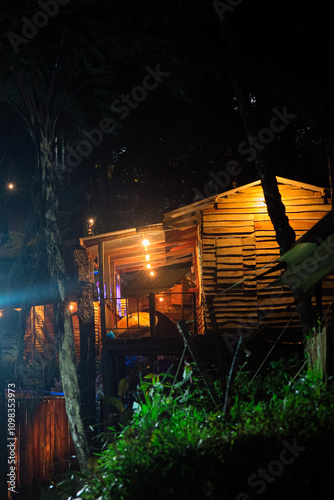 Photos A cozy wooden cabin illuminated by warm lights, nestled amidst lush greenery
