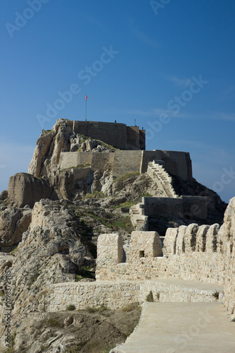 Ancient Van Castle in Turkey, known also as Tushba Castle (Van Kalesi) with the background of panoramic view of Van City and snowy Erek Mountain. Flying Turkish flag and mosque on top of Van Castle.