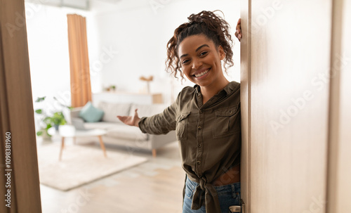 Welcome To My Home. Joyful Millennial Black Lady Opening Door And Gesturing Inviting To Come In Standing Indoors, Smiling To Camera. Real Estate Owner. Hospitality Concept