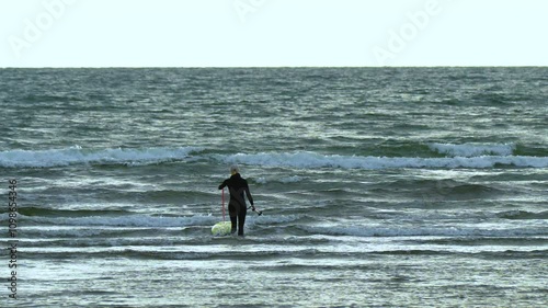 Person entering the water with a foil board and a paddle