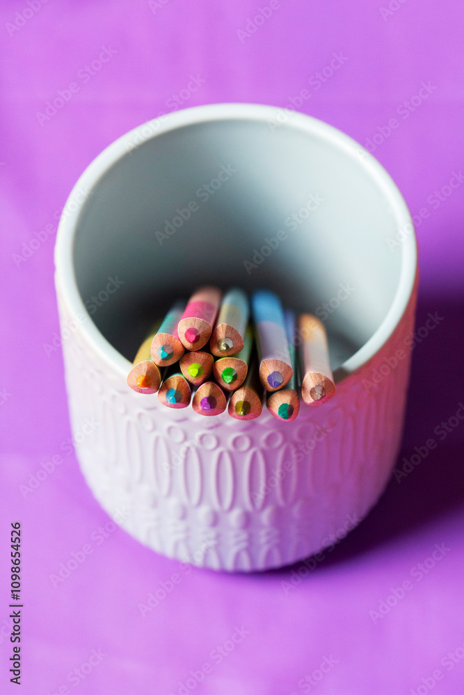 Sharpened pastel colored pencils in a ceramic cup on a colored background for drawing.