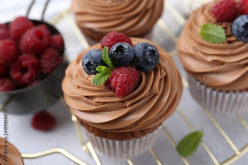 Foto Tasty cupcakes with chocolate cream and berries on white table, closeup