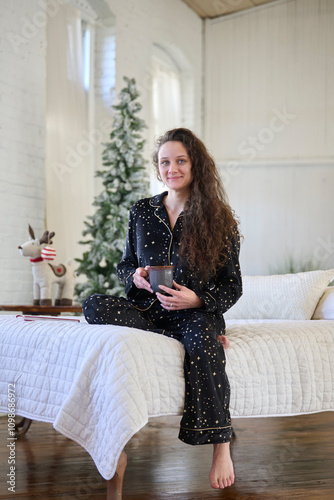 Cute young woman sits in bed in warm pajamas and barefoot - Christmas photo