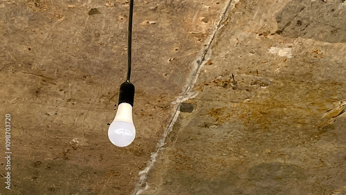 A light bulb hanging from the ceiling. The light bulb is white and is hanging from a cord