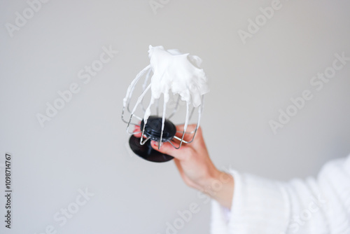 Metal whisk with whipped egg whites on white background photo