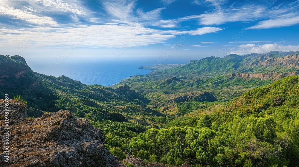 Fototapeta premium Stunning panoramic view of lush green mountains transitioning into a serene coastline under a bright blue sky with scattered clouds.