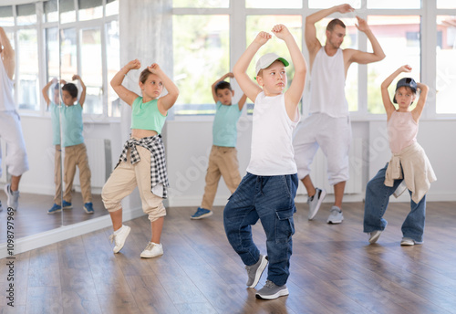 Preteen boy performing hip hop dance moves, showcasing skills and concentration, during group class for kids led by young male instructor in street dance studio photo