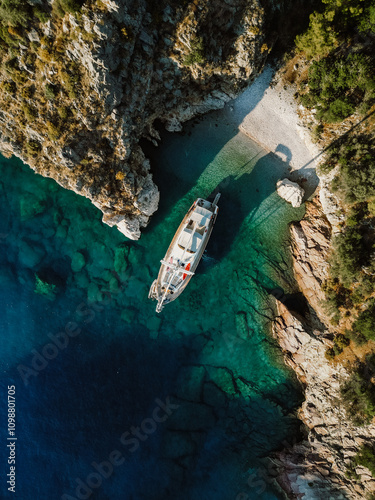 Photography A stunning aerial view of a secluded cove with turquoise waters, rugged cliffs, and a luxury sailing yacht anchored near a small, hidden beach