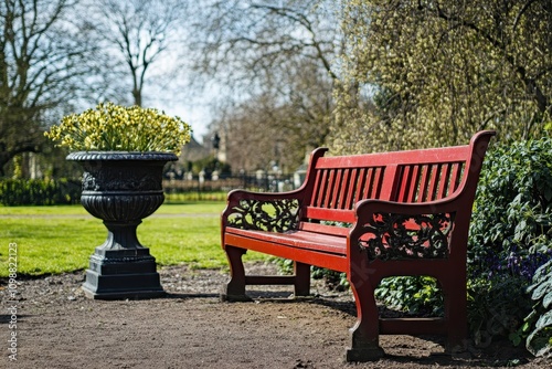 A sizable vacant bench in an urban park or garden featuring a red wooden bench and a metal urn