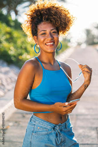 Young woman holding sunglasses is smiling outdoors