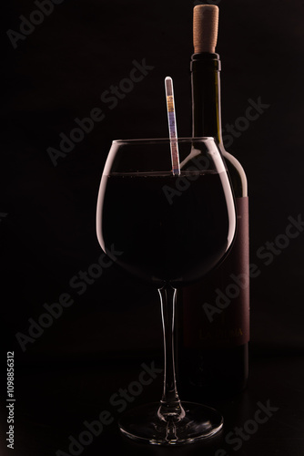transparent glass goblet with wine and bottle of wine with cork on black background