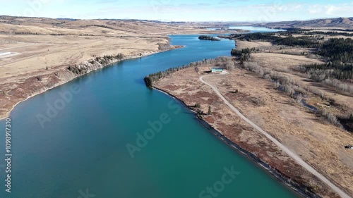 Aerial flight down river valley overlooking small town with golf course and waterfront homes along a bridge with Vehicle Traffic.
