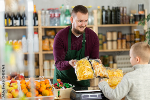 Young male seller offers crispy chips to boy buyer in grocery store photo