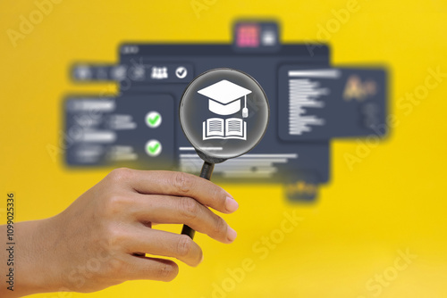 A hand holding a magnifying glass over a computer screen with a graduation cap