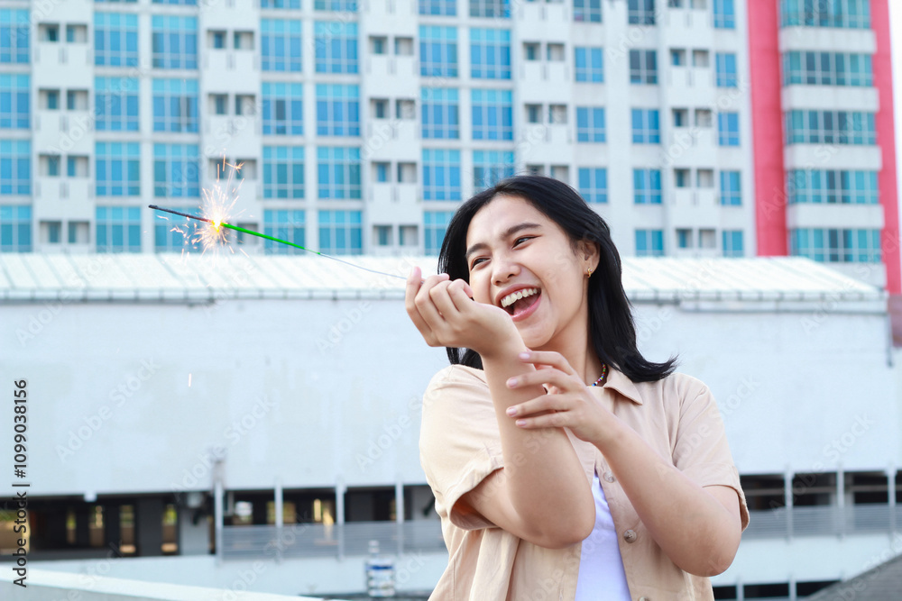 Fototapeta premium happy asian young woman holding sparklers celebrate new year eve in outdoor roof top with city building background
