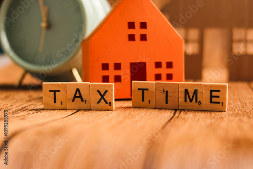 A vintage alarm clock set to 12 o'clock, positioned alongside paper house models and letter tiles spelling out 