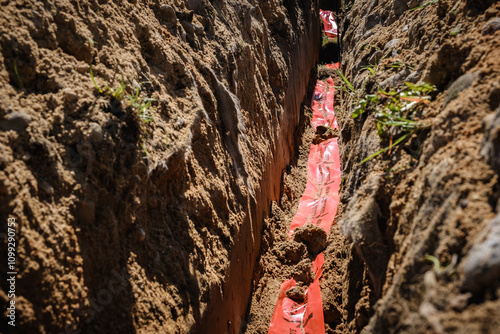 Warning tape with the words Attention cable and the same text in Russian translation words. Marked underground cables in the trench. Laying out infrastructure communications. Vertical photo photo