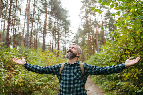 Handsome man standing in the middle of nature with open arms and closed eyes. Peaceful atmosphere of the forest, forestbathing. photo