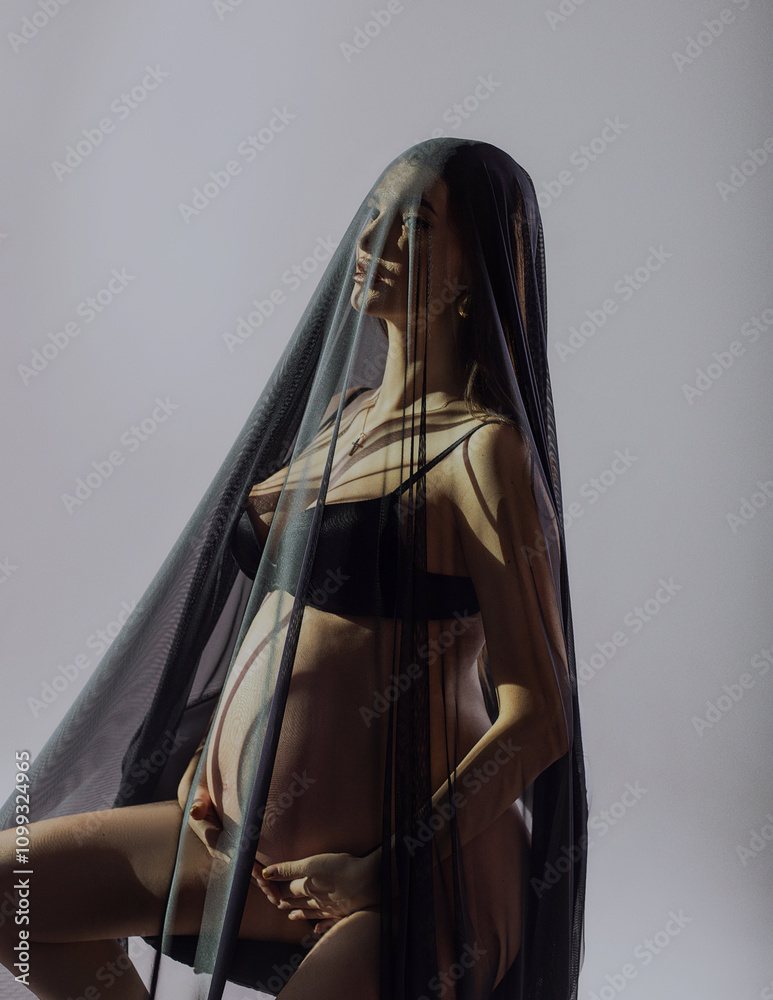Naklejka premium beautiful pregnant woman in studio under dark veil like virgin mary
