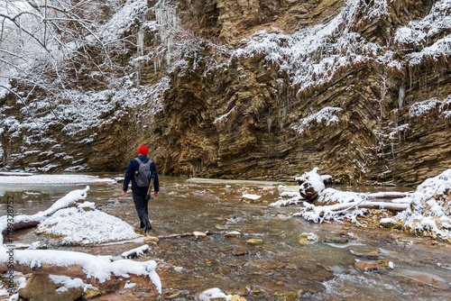 A male photographer, a traveler with a backpack, walks along the Rufabgo creek in the winter forest photo