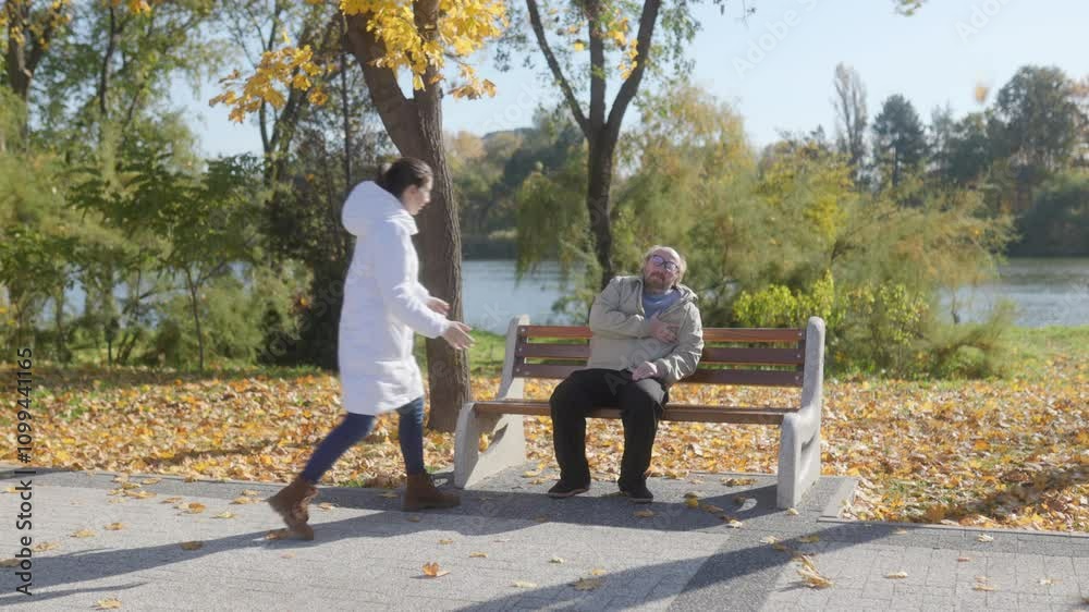 Senior man in distress on park bench, concerned woman stops to assist