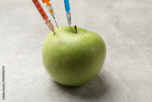 GMO concept. Green apple with different syringes on grey textured table, closeup