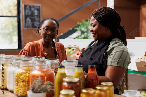 African american women at local store looking at jars filled with sustainable organic products. Shopkeeper assisting customer with choosing chemical free nutritious food items for healthy lifestyle. photo