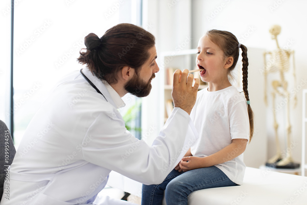 Obraz premium Caucasian male doctor examines throat of girl with tongue depressor in modern medical clinic. Scene portrays professional healthcare setting emphasizing doctor-patient interaction, diagnosis.