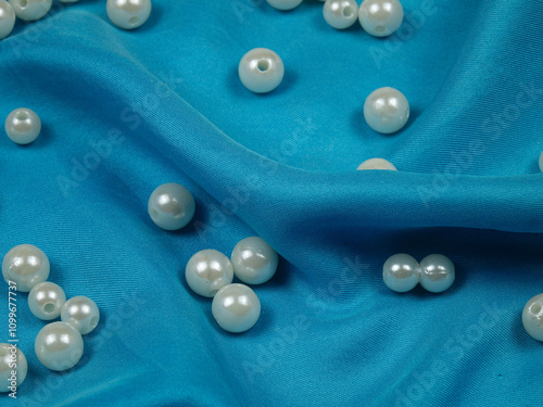 White pearl beads lie on turquoise natural silk fabric, background
