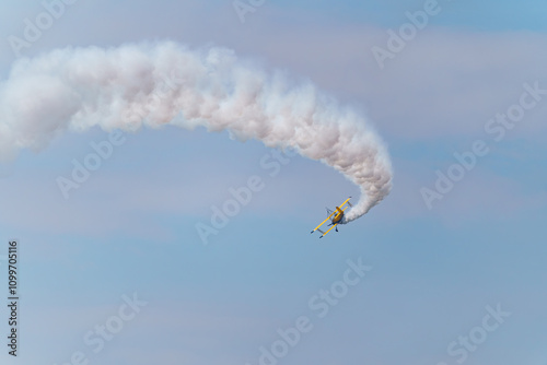 Foto A yellow biplane performing maneuvers at an air show, leaving a smoke trail behind