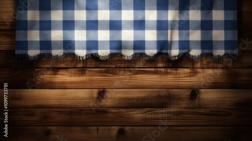 Blue and white checked tablecloth edge draped over a rustic dark wooden surface, accentuating kitchen textile elements with a cozy feel. photo