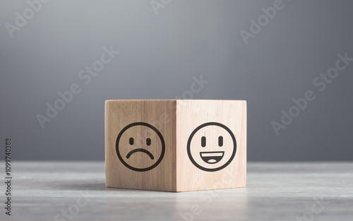 Wooden blocks displaying a sad face transitioning to a happy face, symbolizing a shift from negativity to positivity. Final block turns from sad to happy, highlighting the power of a positive outlook photo