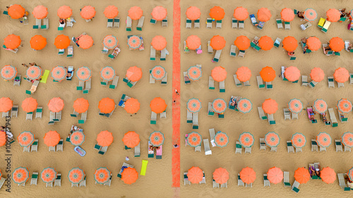 Perpendicular aerial view of a beach club with orange umbrellas and people on vacation. The coast is sandy.