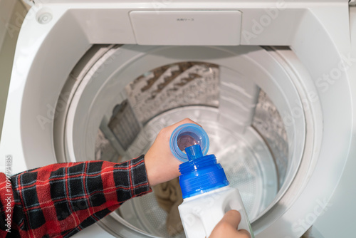 洗濯用洗剤をカップに入れる人物の手元と洗濯機