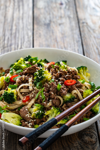 Udon noodles with minced beef and broccoli on wooden table