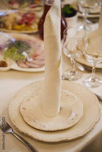 A served festive table with white plates and a cloth napkin. Beautiful serving of dishes at a banquet.