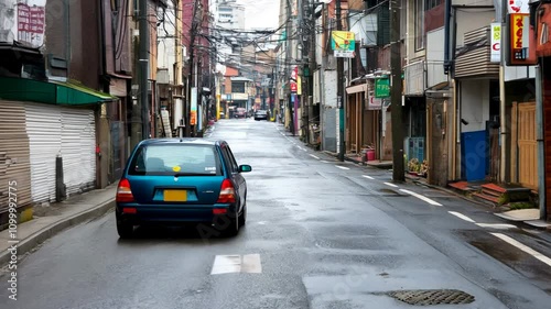 Blue hatchback vehicle driving in suburban Japanese neighborhood. Turquoise car in messy downtown residential district of Nagoya. Transportation in Japan. Automotive transportation in Asian countries.