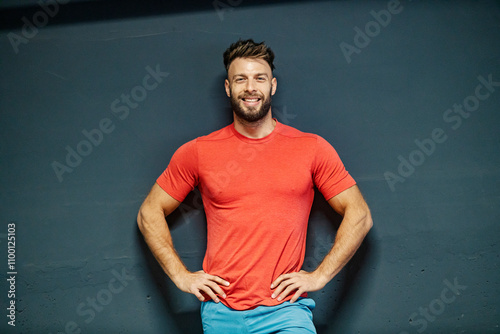 Portrait of a happy healthy fit muscular sportsman standing against the wall with hands on hips and smiling at camera.